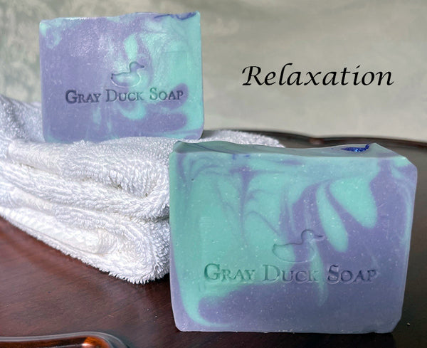 Two  bar s of Relaxation blue and purple soap with Gray Duck Soap stamp displayed on a towel.